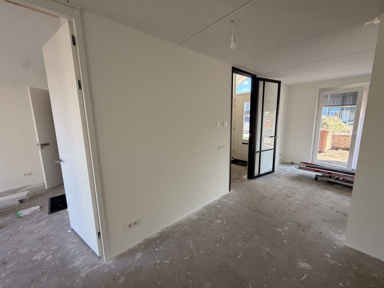 Hal van een nieuwbouwwoning met renovlies en een zwarte stalen deur naar de woonkamer